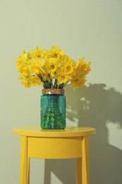 Beautiful daffodils in vase on table near light green wall