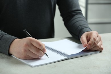 Man writing with pen in notebook at white table, closeup