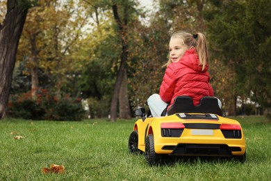 Cute little girl driving children's car in park, back view. Space for text