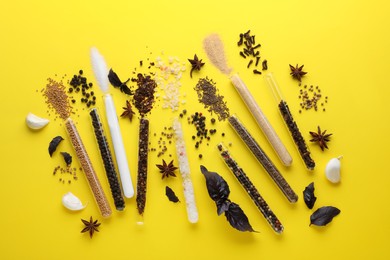 Photo of Glass tubes with different spices on yellow background, flat lay