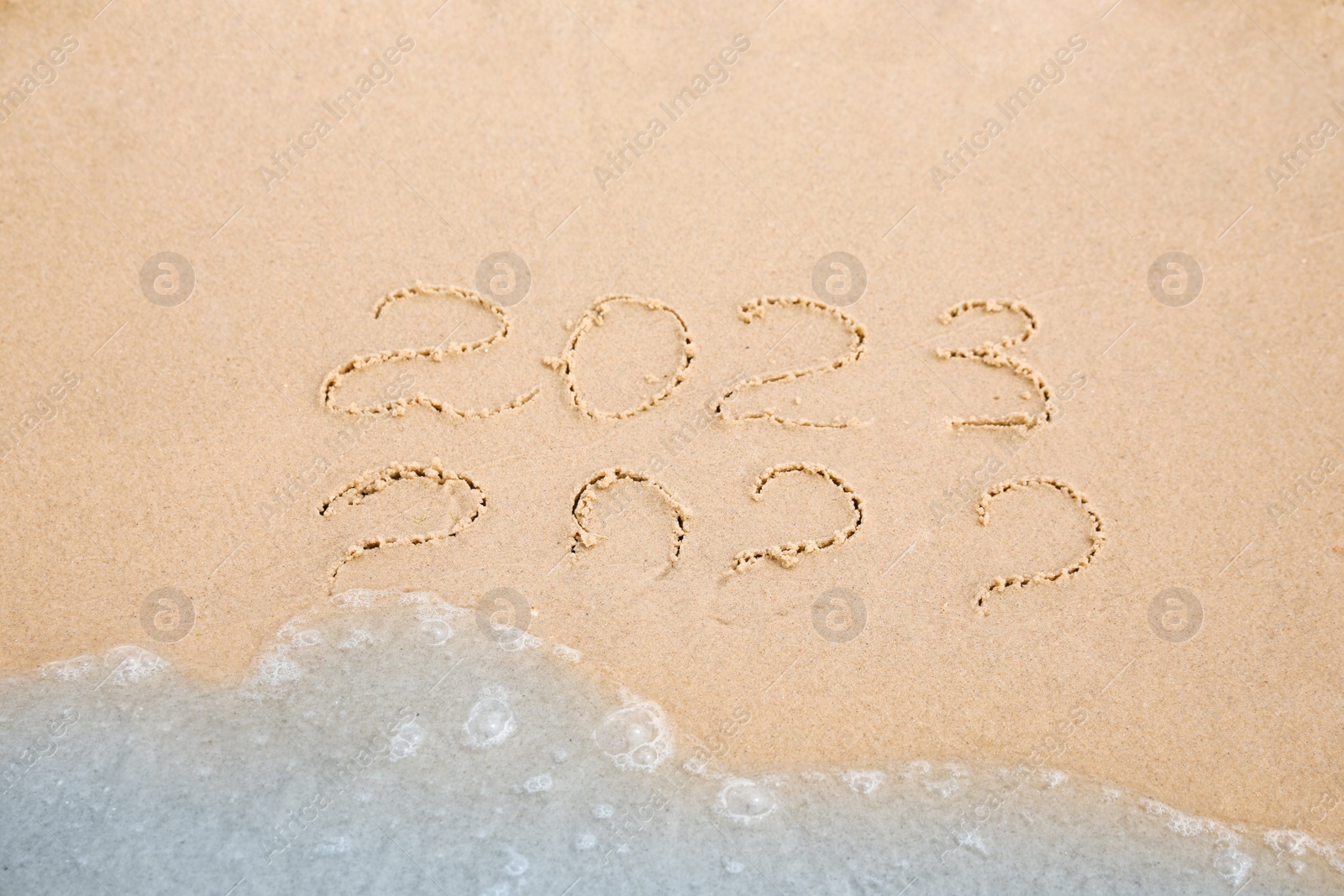 Photo of Dates written on sandy beach. 2022 washed by sea wave as New 2023 Year coming