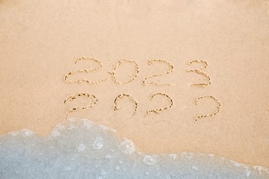 Photo of Dates written on sandy beach. 2022 washed by sea wave as New 2023 Year coming