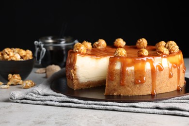 Photo of Sliced delicious cheesecake with caramel and popcorn on light grey table, closeup. Space for text