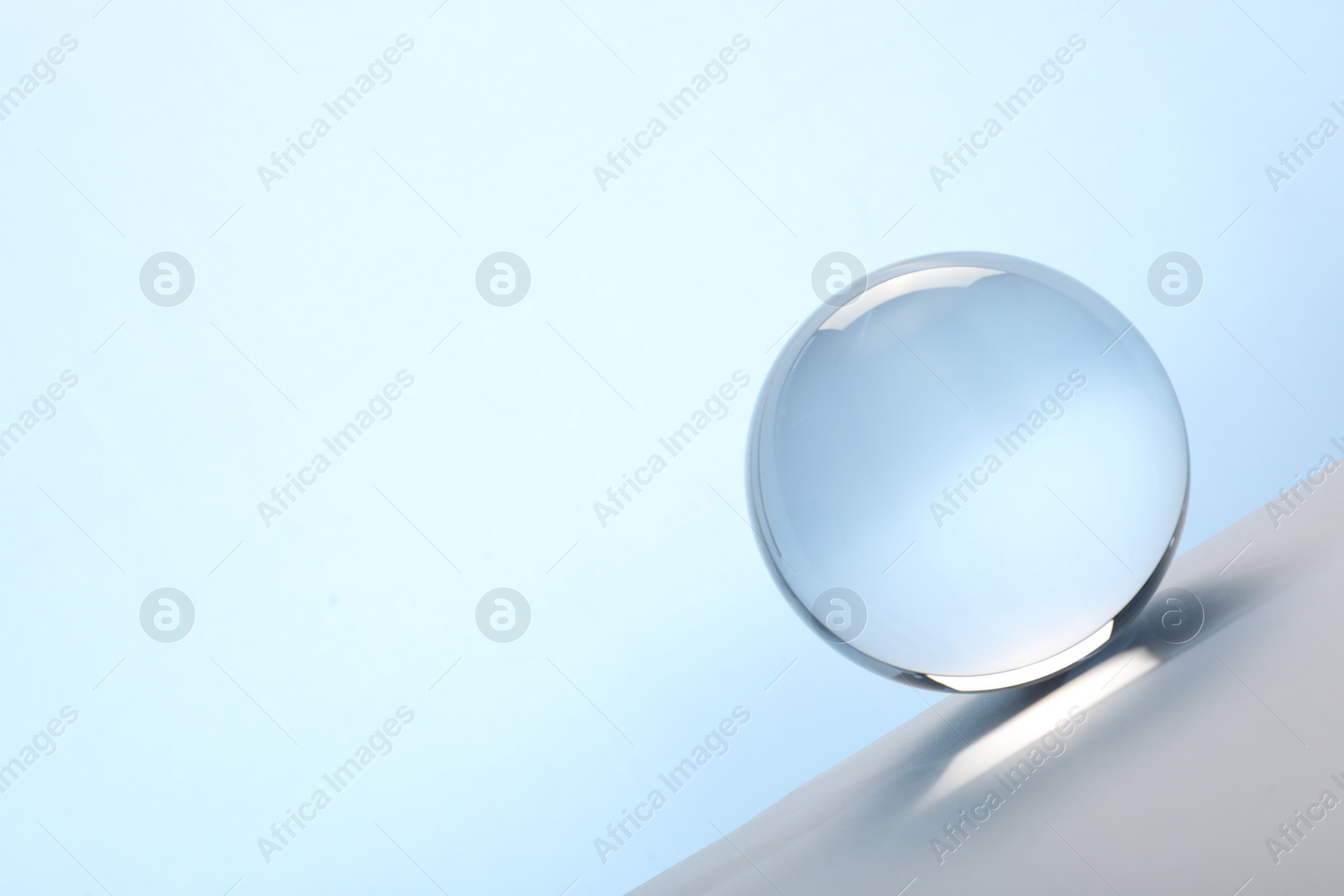 Photo of Transparent glass ball on table against light blue background. Space for text