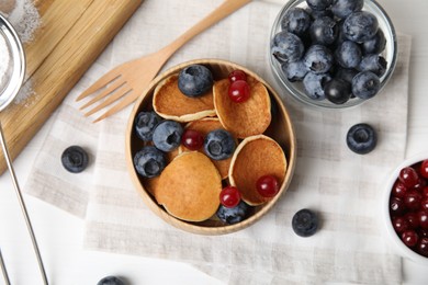 Photo of Delicious mini pancakes cereal with berries served on white table, flat lay