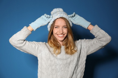 Happy young woman wearing warm sweater, knitted hat and mittens on blue background