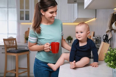 Happy young woman and her cute little baby spending time together in kitchen