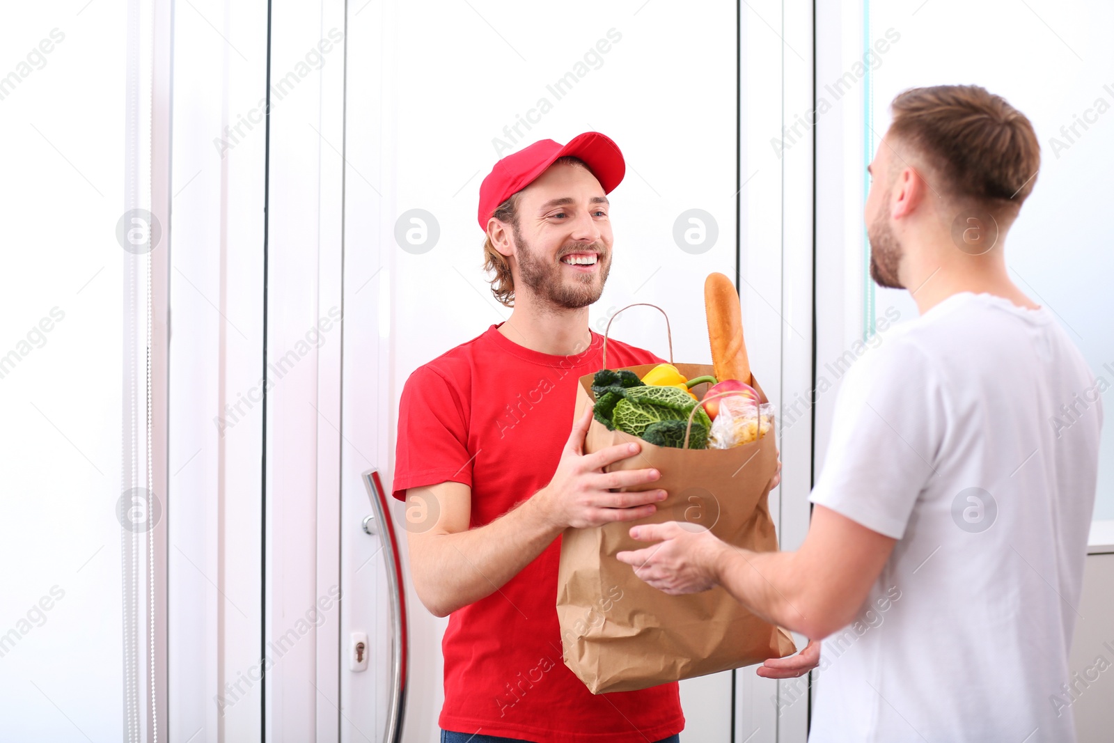 Photo of Courier giving paper bag with products to customer at home. Food delivery service