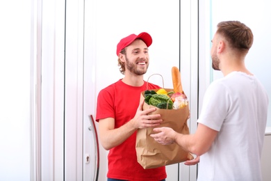 Courier giving paper bag with products to customer at home. Food delivery service