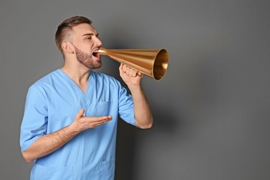 Photo of Male doctor shouting into megaphone on grey background