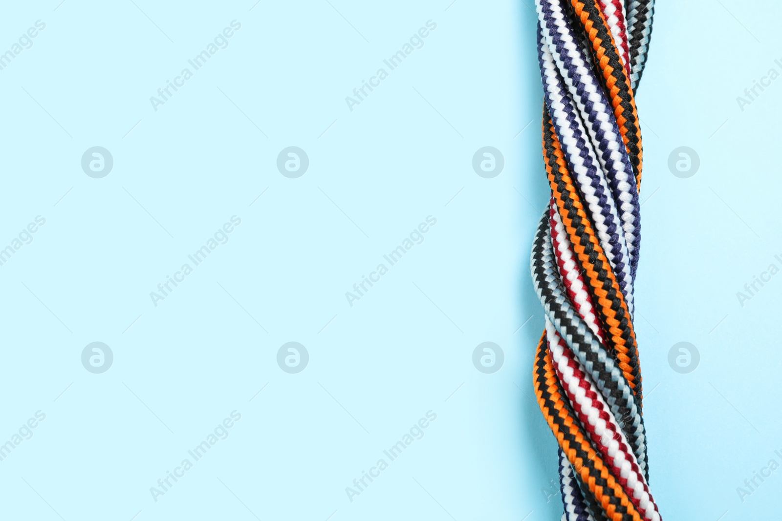 Photo of Top view of twisted colorful ropes on light blue background, space for text. Unity concept