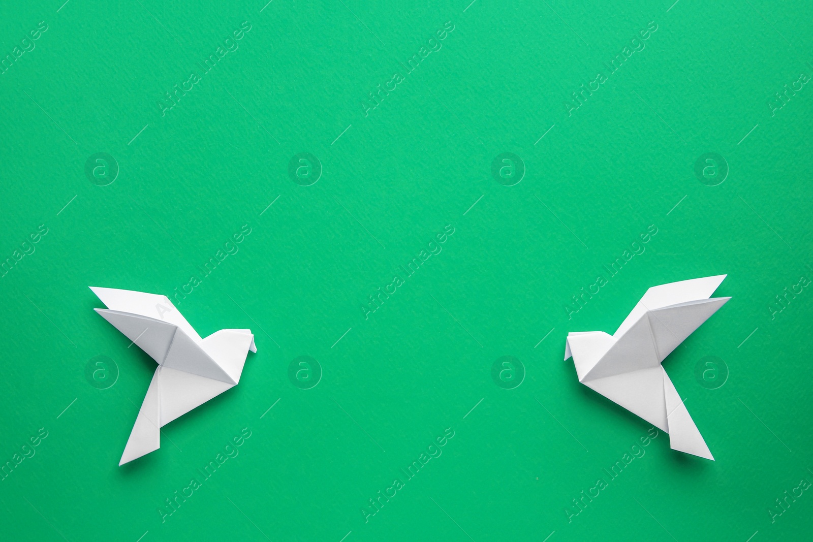 Photo of Beautiful white origami birds on green background, flat lay. Space for text