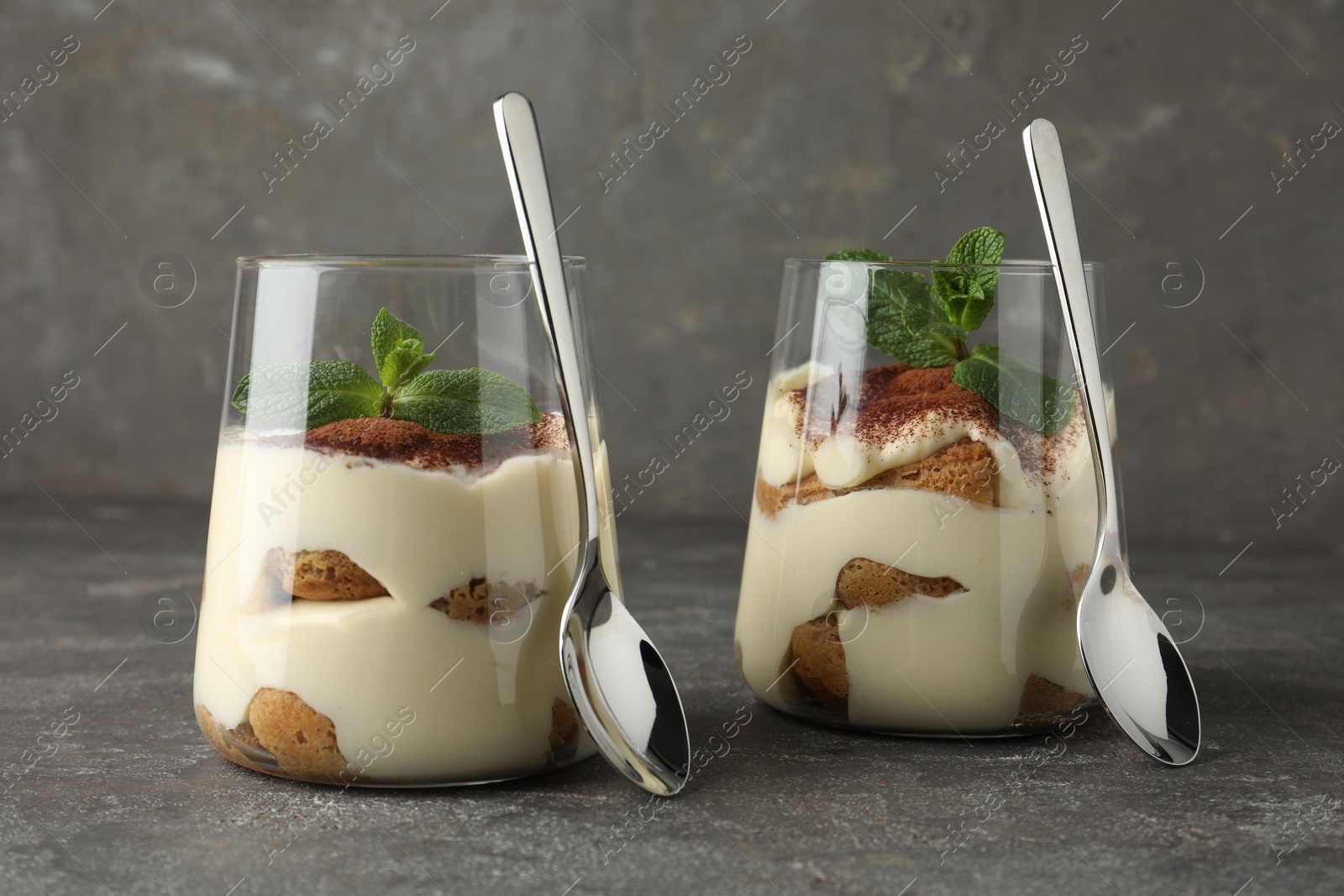 Photo of Delicious tiramisu with mint in glasses on grey table