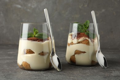 Delicious tiramisu with mint in glasses on grey table