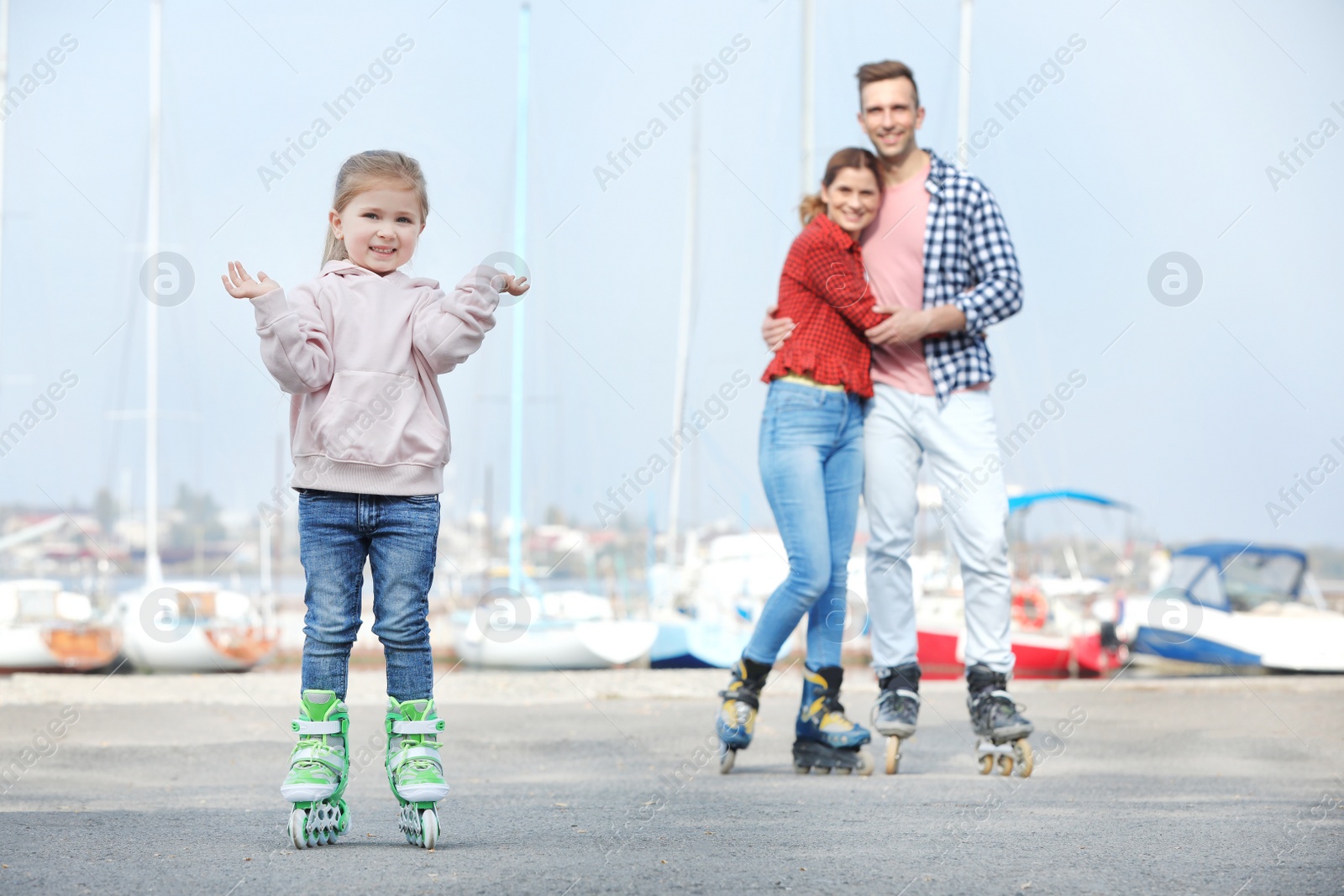 Photo of Little girl and her parents roller skating on embankment