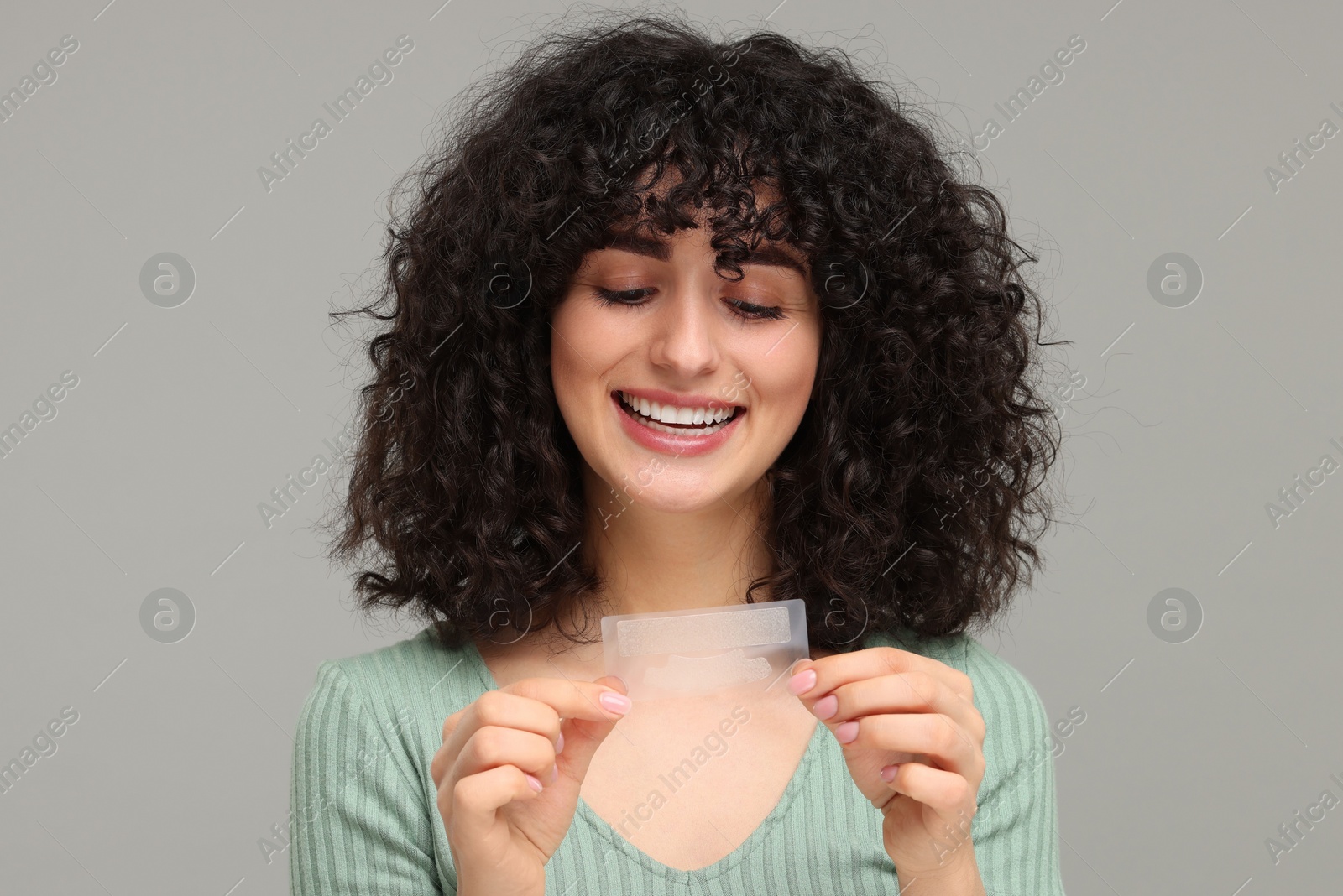 Photo of Young woman holding teeth whitening strips on grey background