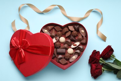 Photo of Heart shaped box with delicious chocolate candies, roses and ribbon on light blue background, flat lay