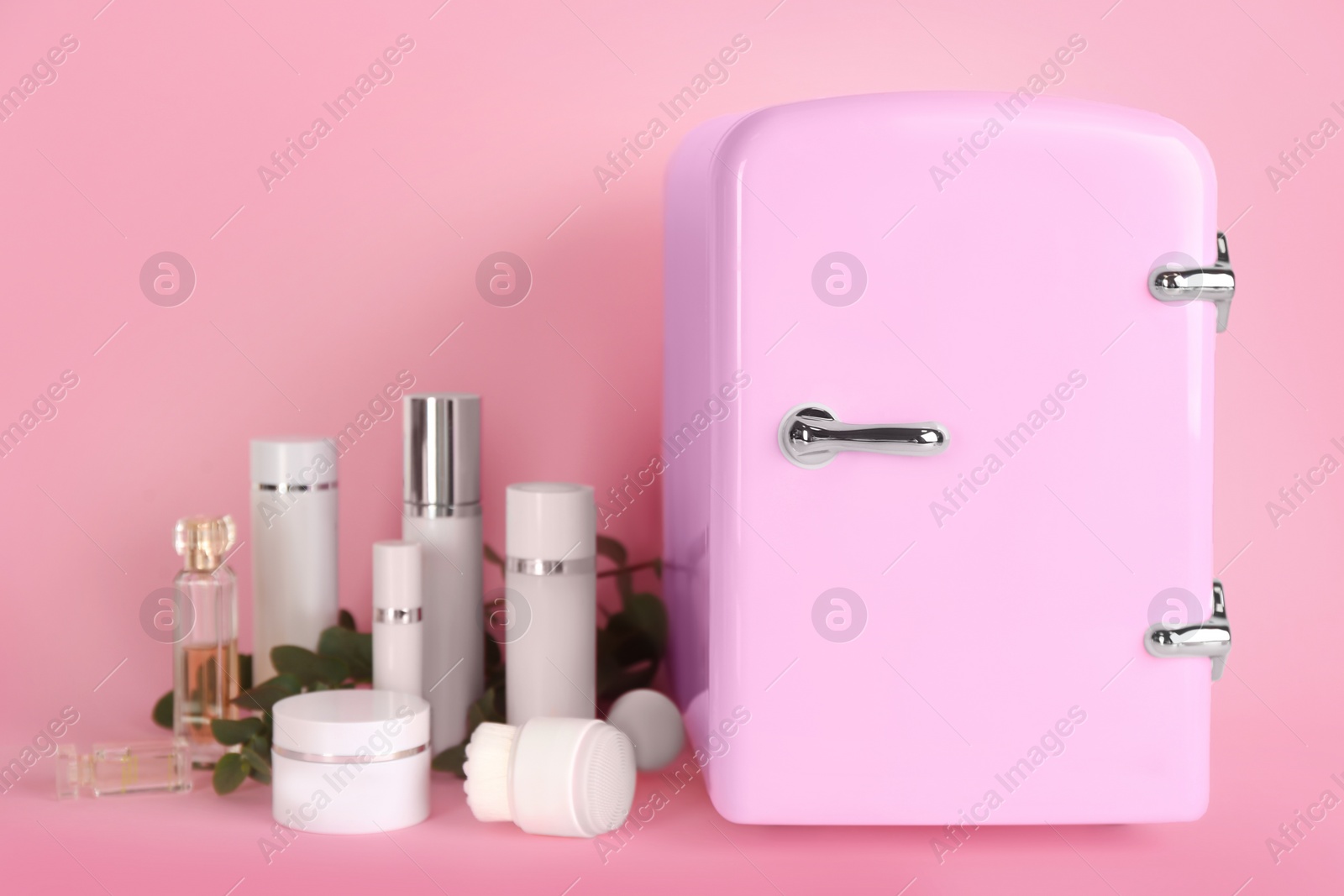 Photo of Cosmetic refrigerator and skin care products on pink background