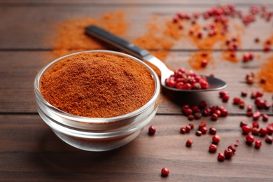 Photo of Bowl of red powdered pepper and spoon with corns on wooden table, space for text