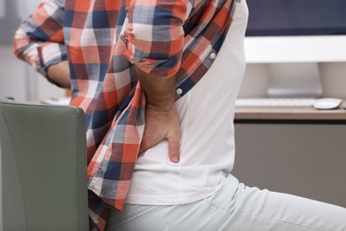 Young man suffering from back pain in office, closeup