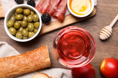 Photo of Glass of delicious rose wine and snacks on wooden table, flat lay