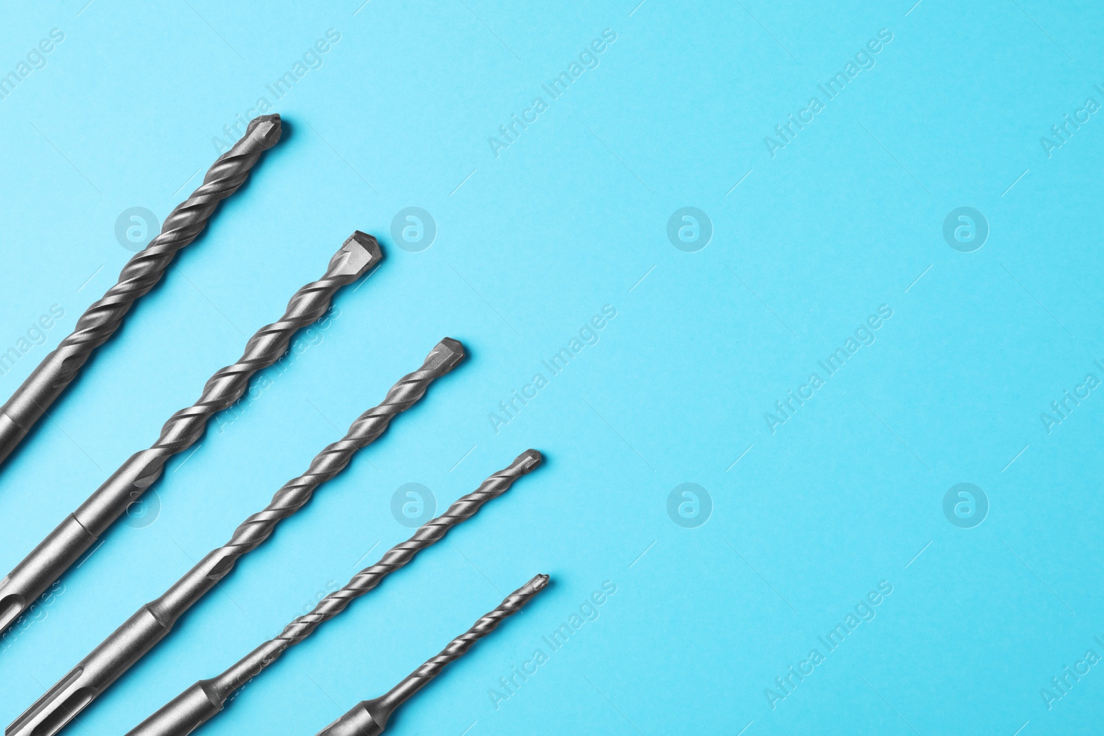 Photo of Different drill bits on light blue background, flat lay. Space for text