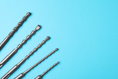 Photo of Different drill bits on light blue background, flat lay. Space for text