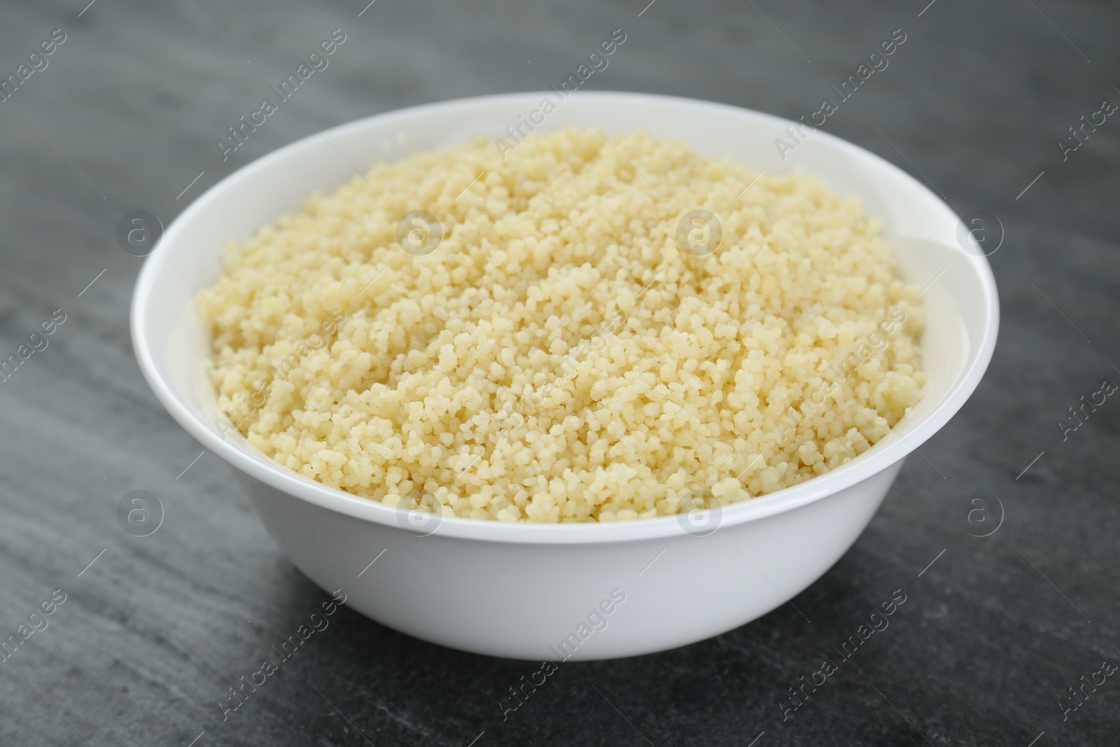 Photo of Bowl of tasty couscous on grey table, closeup