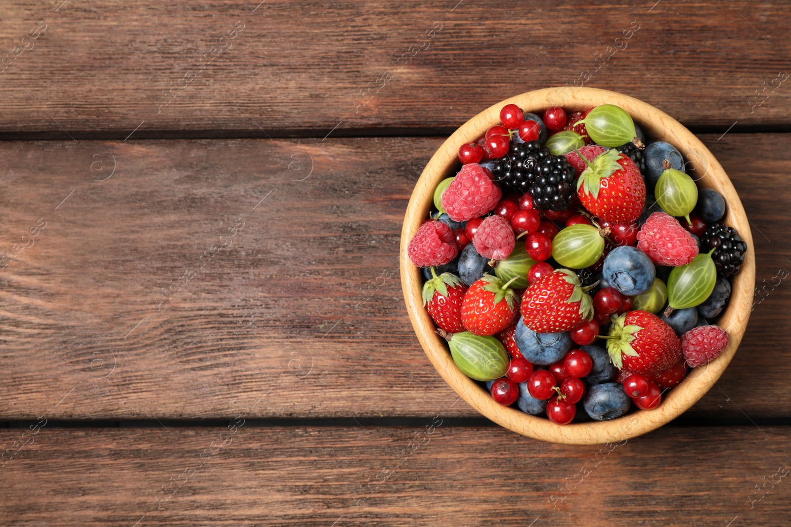 Photo of Mix of ripe berries on wooden table, top view. Space for text