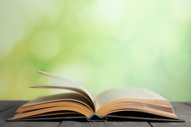 Open book on blue wooden table against blurred green background. Space for text