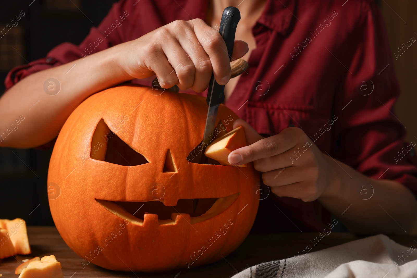 Photo of Woman carving pumpkin for Halloween at wooden table, closeup