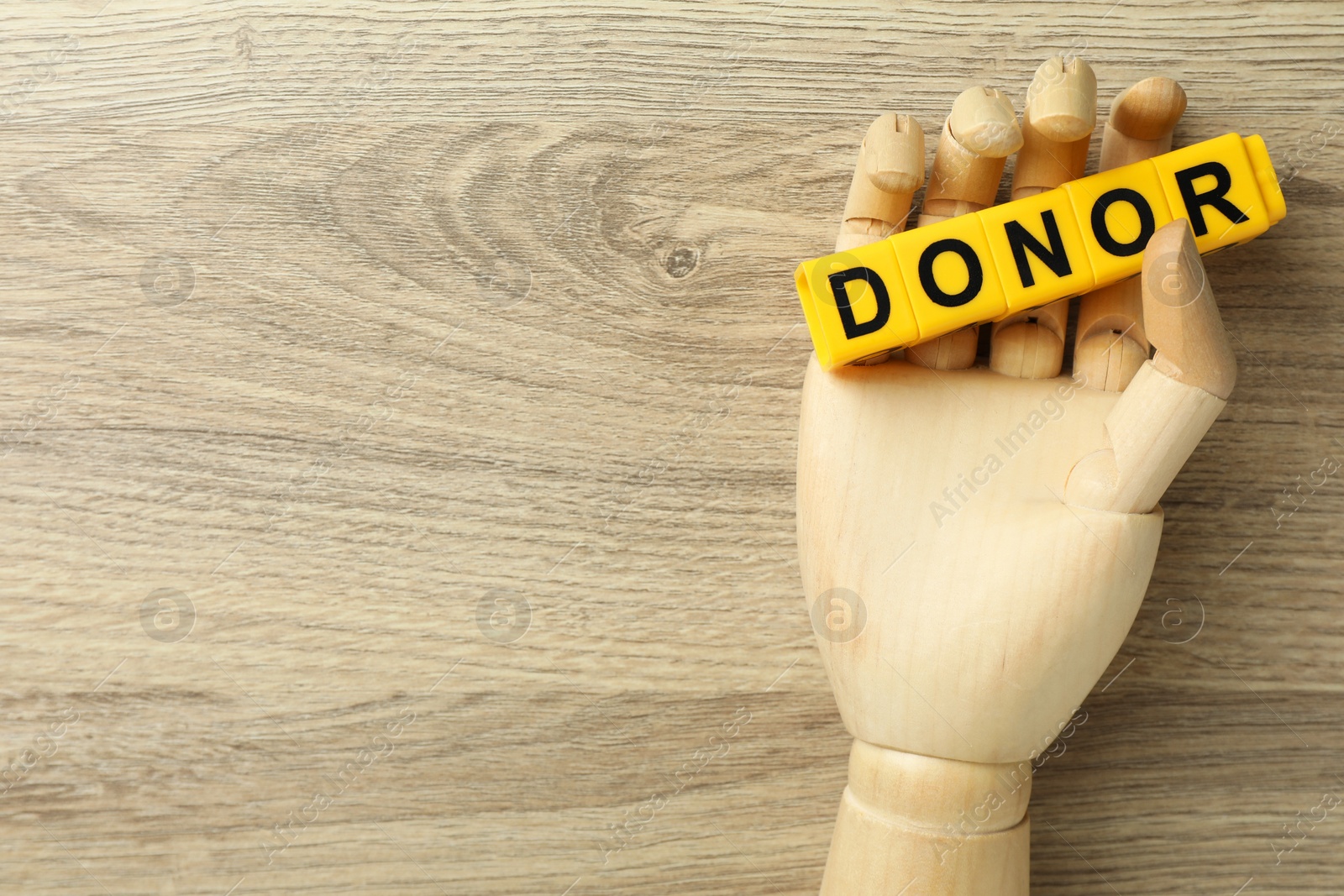 Photo of Mannequin hand holding word Donor made of cubes on wooden table, top view. Space for text