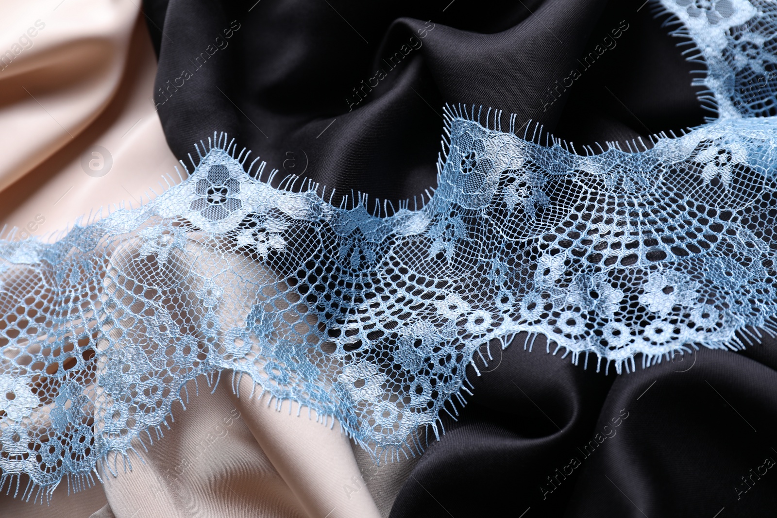 Photo of Beautiful light blue lace on color fabrics, closeup