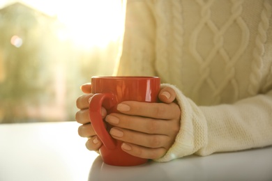 Woman holding elegant cup at table indoors, closeup