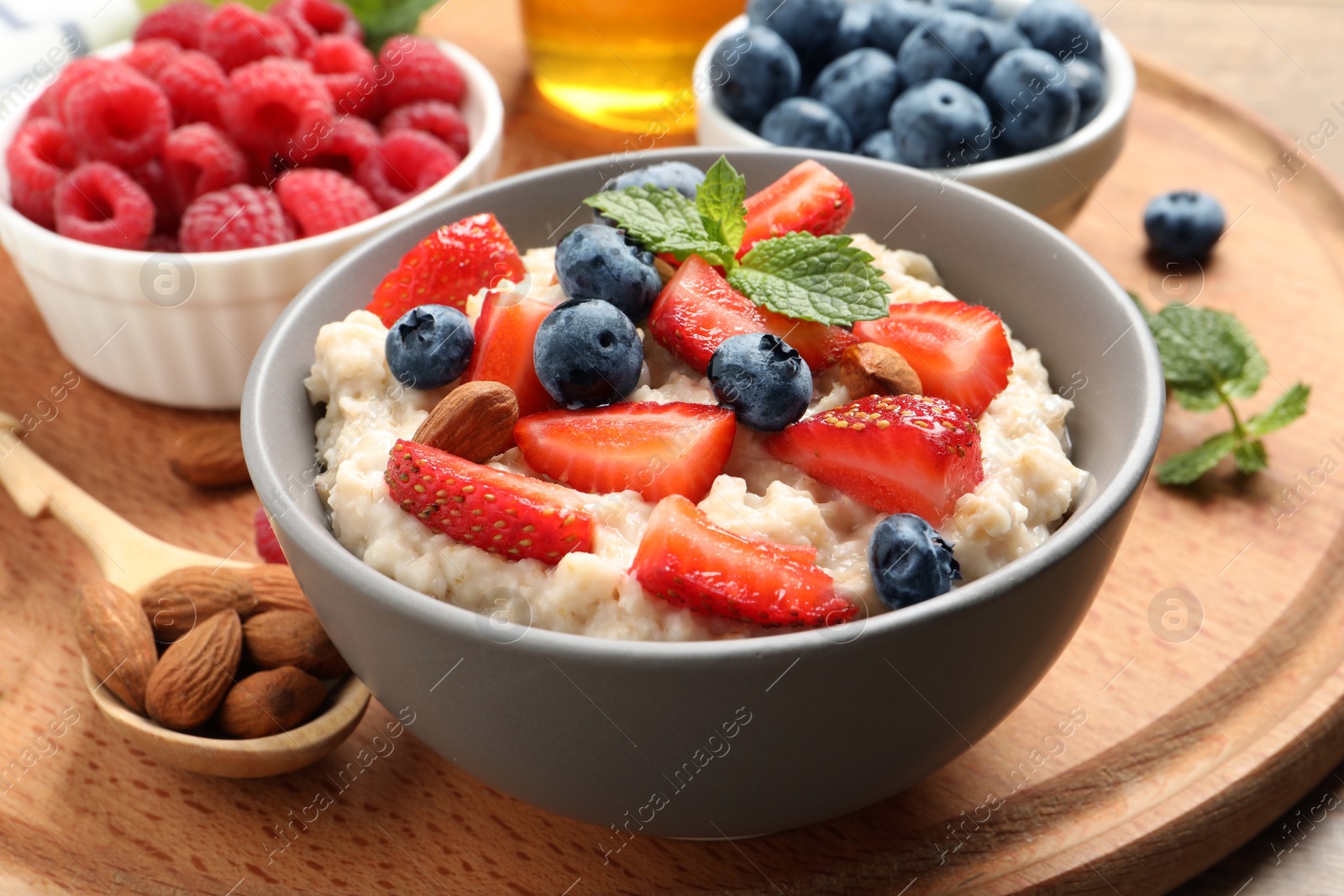 Photo of Tasty oatmeal porridge with berries and almond nuts served on wooden board