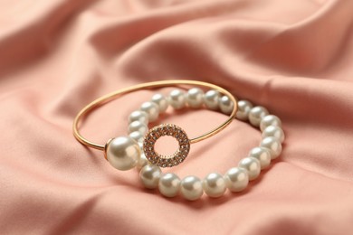 Photo of Elegant bracelets with pearls on pink silk, closeup