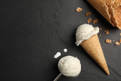 Ice cream scoops in wafer cones on dark gray textured table, flat lay. Space for text