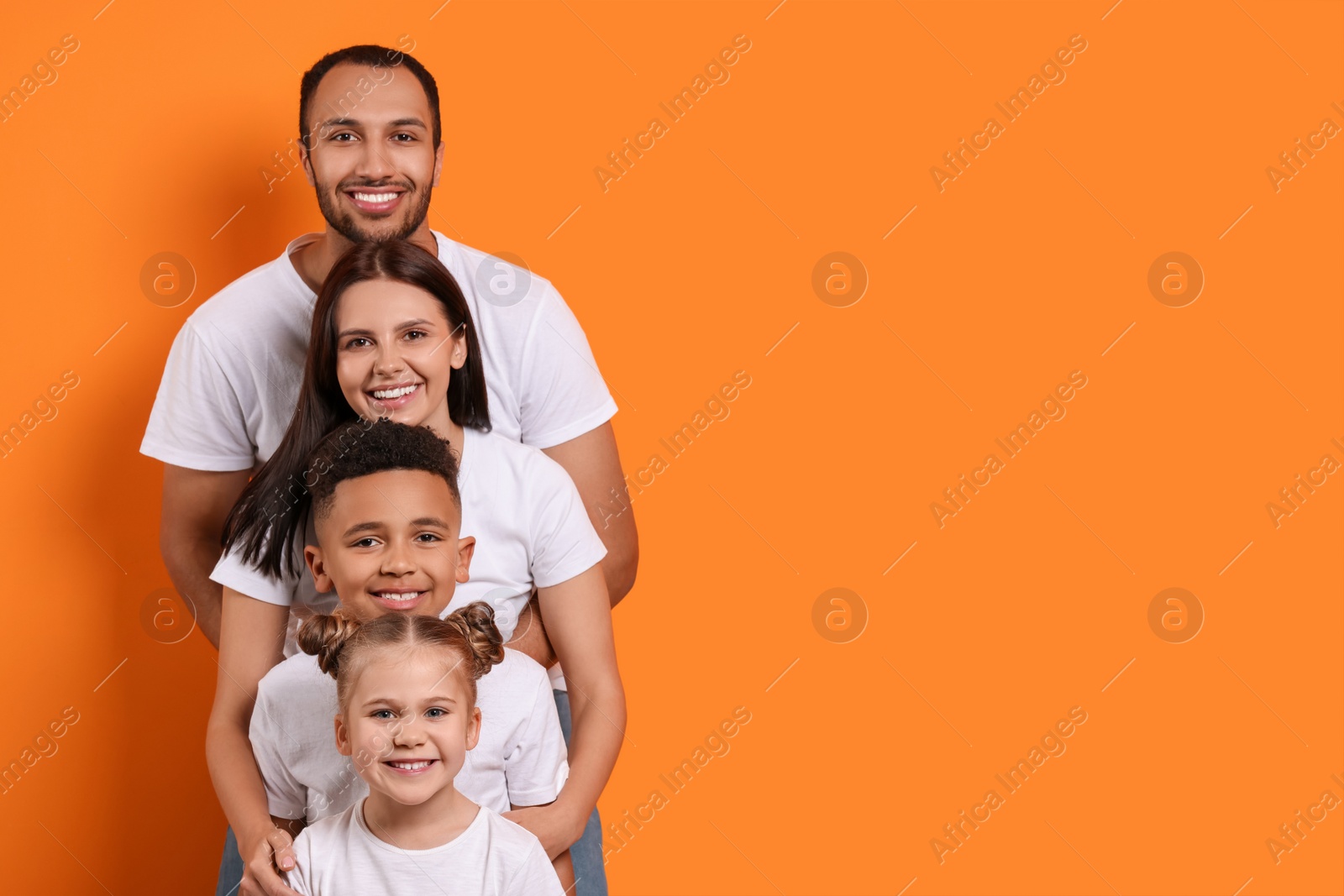 Photo of Happy international family with children on orange background. Space for text