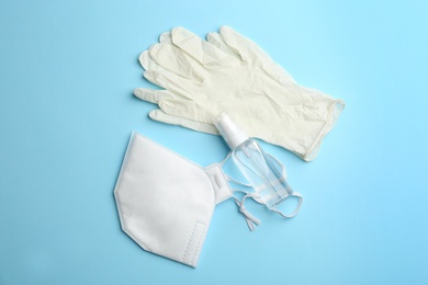 Photo of Medical gloves, respirator and hand sanitizer on light blue background, flat lay