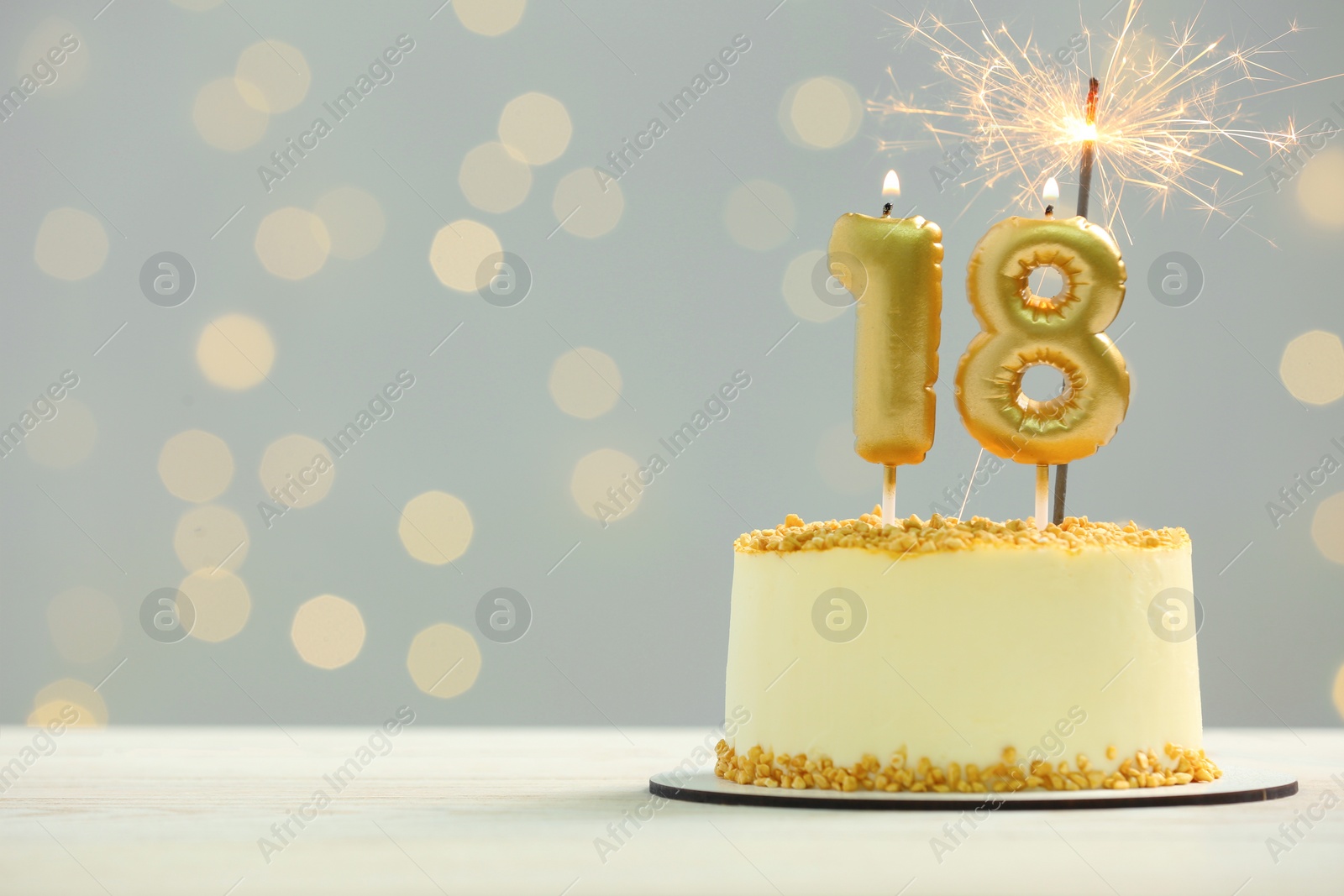 Photo of Coming of age party - 18th birthday. Delicious cake with number shaped candles and sparkler on white table against blurred lights, space for text