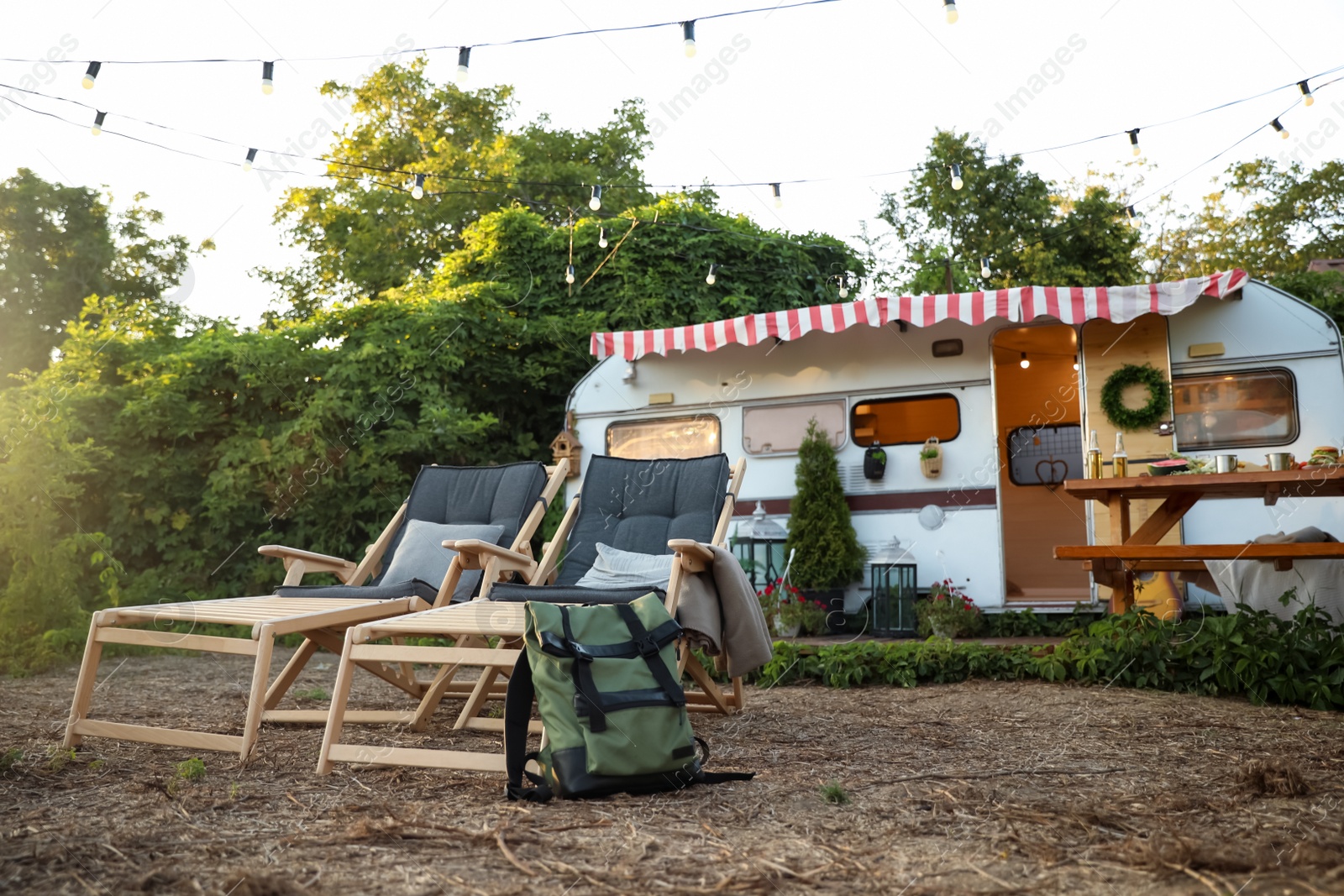 Photo of Deck chairs and backpack near modern trailer. Camping season