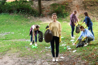 Photo of Young woman with plastic bag and group of people collecting garbage in park