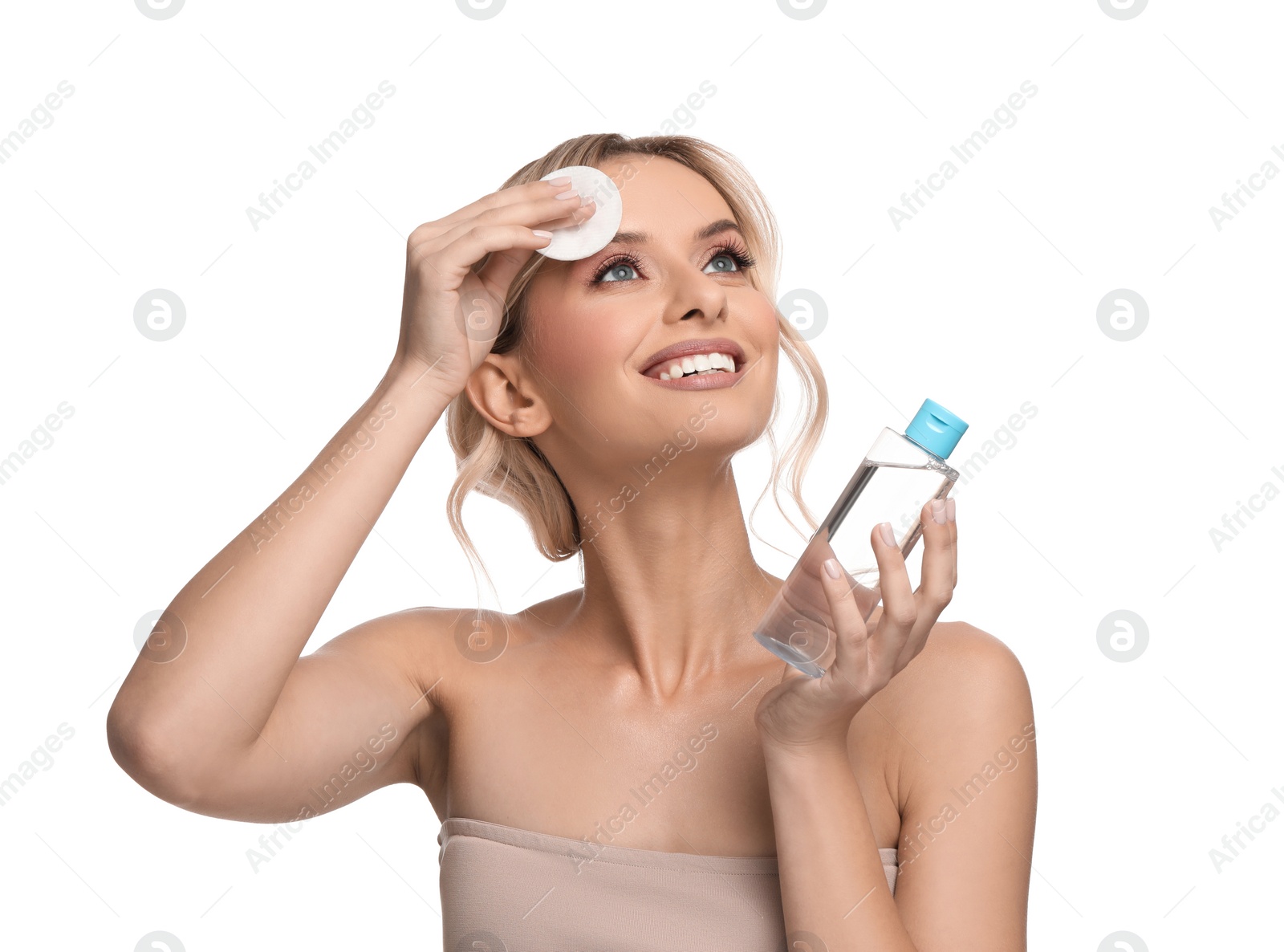 Photo of Smiling woman removing makeup with cotton pad and holding bottle on white background