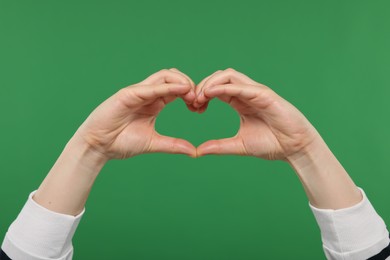 Woman showing heart gesture with hands on green background, closeup