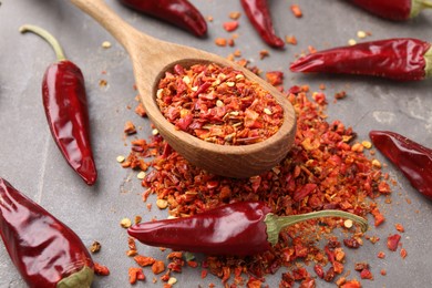 Photo of Chili pepper flakes, pods and spoon on grey table, closeup