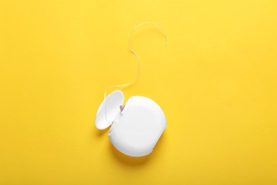 Container with dental floss on yellow background, top view. Space for text