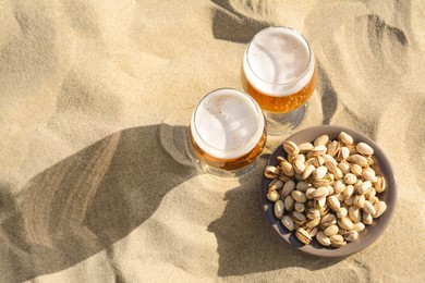 Glasses of cold beer and pistachios on sandy beach, flat lay. Space for text