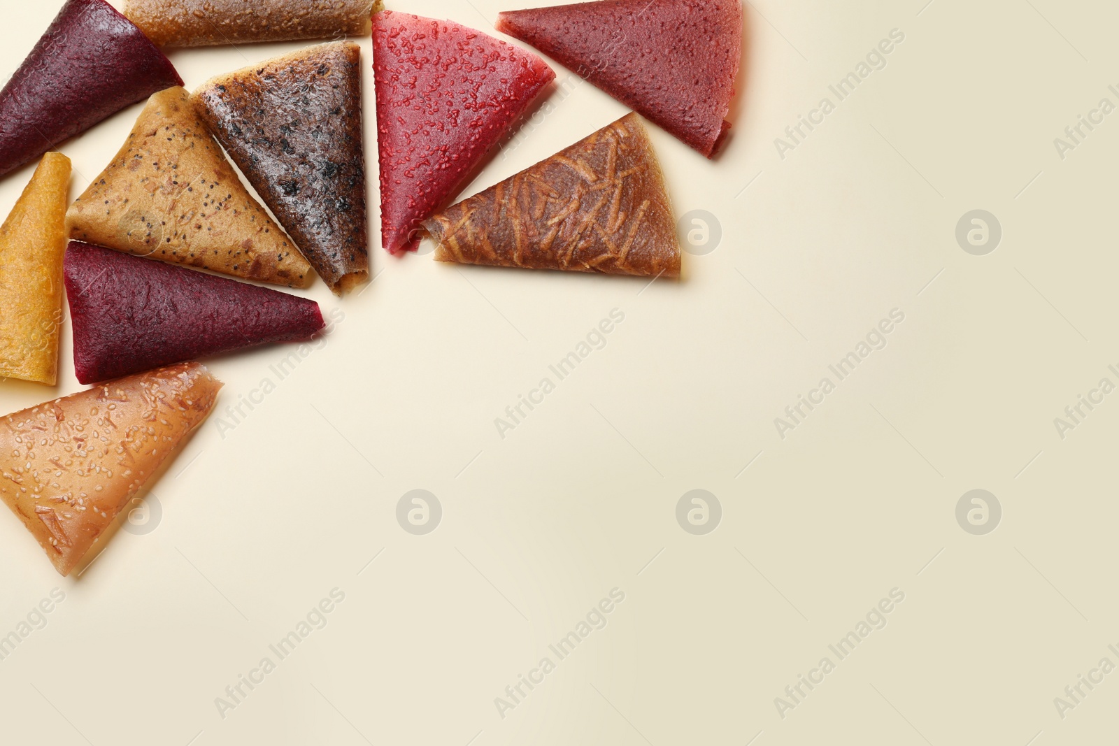 Photo of Delicious fruit leather rolls on beige background, flat lay. Space for text