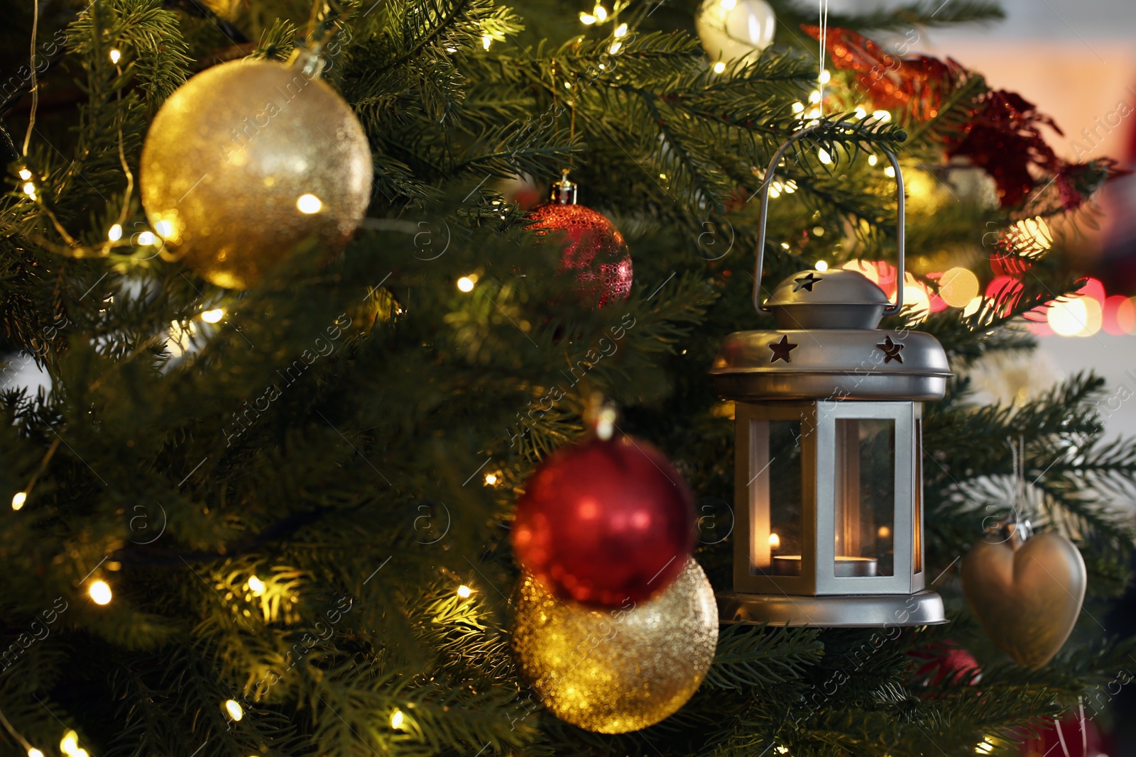 Photo of Christmas lantern with burning candle and balls on fir tree indoors, closeup