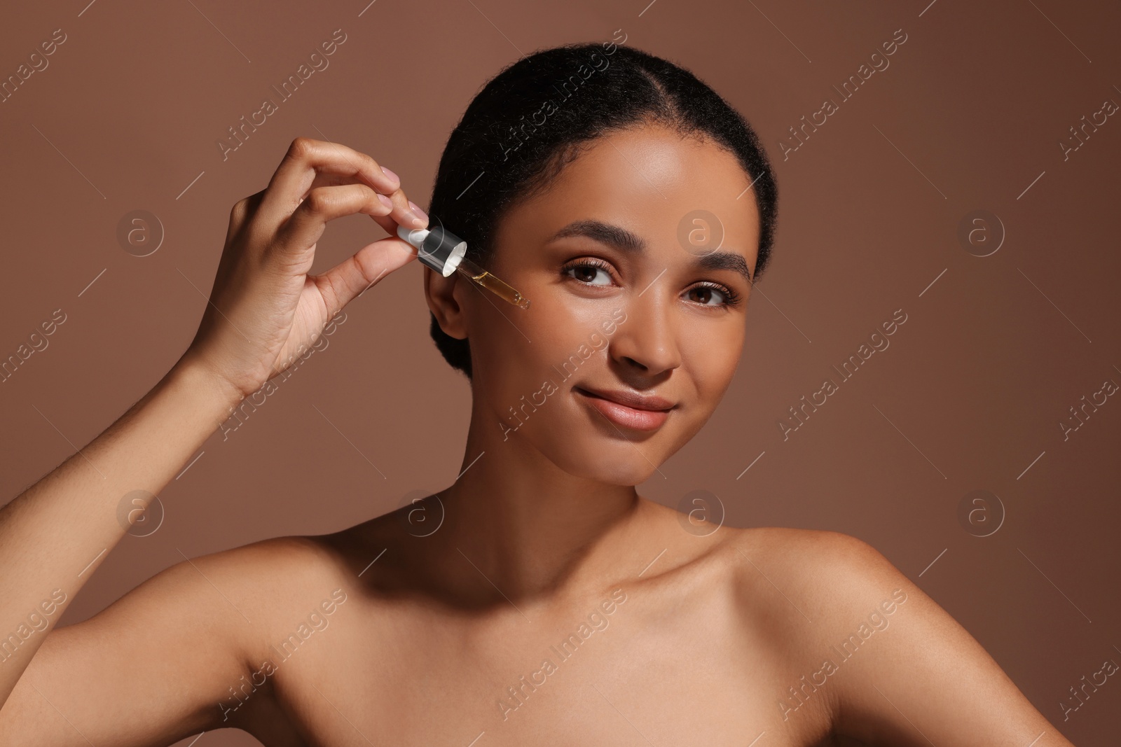 Photo of Beautiful woman applying serum onto her face on brown background